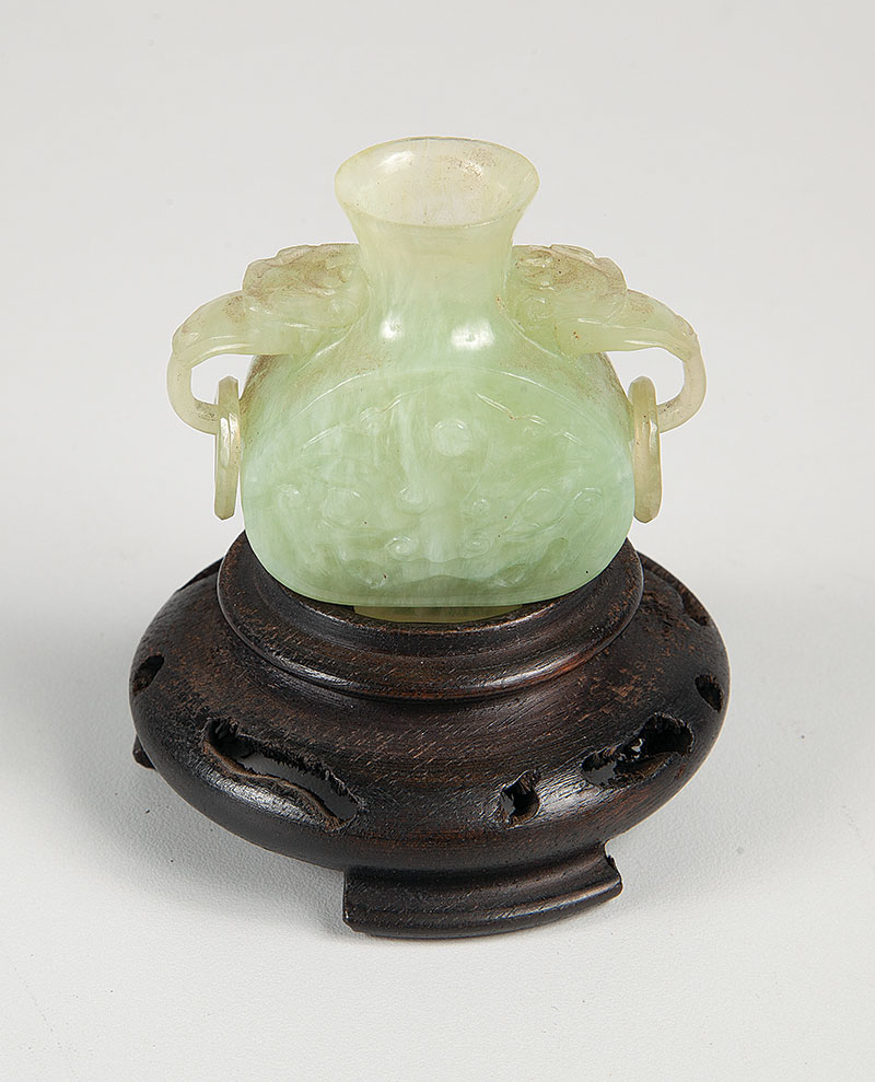 Delicada escultura em jade. - No formato de vaso com alças e base em madeira medindo 5 cm de altura. - China ` Séc. XX.