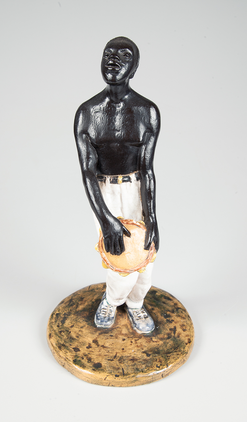 Negro tocando pandeiro de porcelana esmaltada medindo 33 cm. de altura, apresenta nota fiscal da Liceu Artes e oficio datado de 1962.